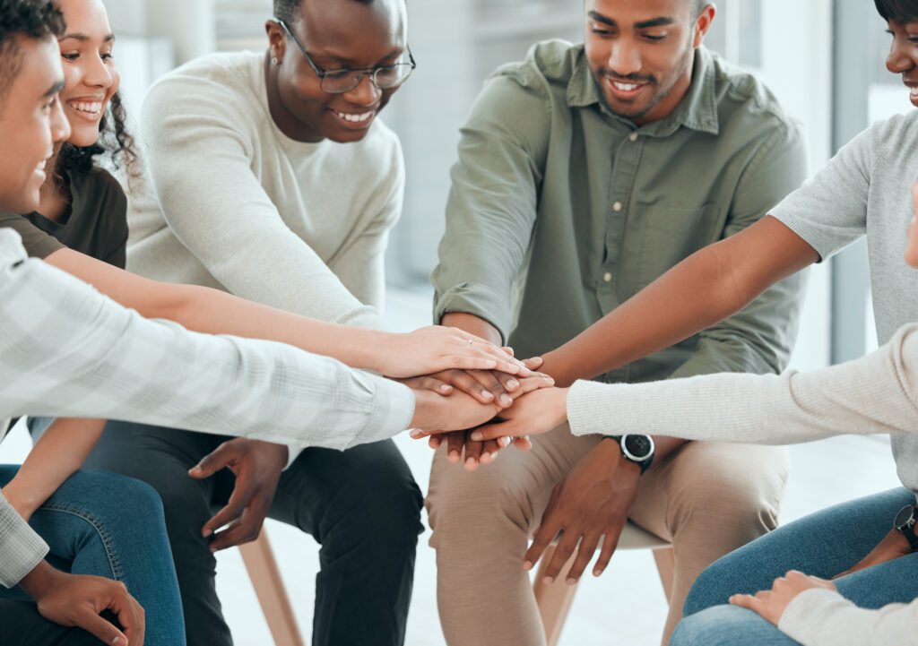 Shot of a diverse group of people sitting together and stacking their hands in the middle at community health improvement plan
